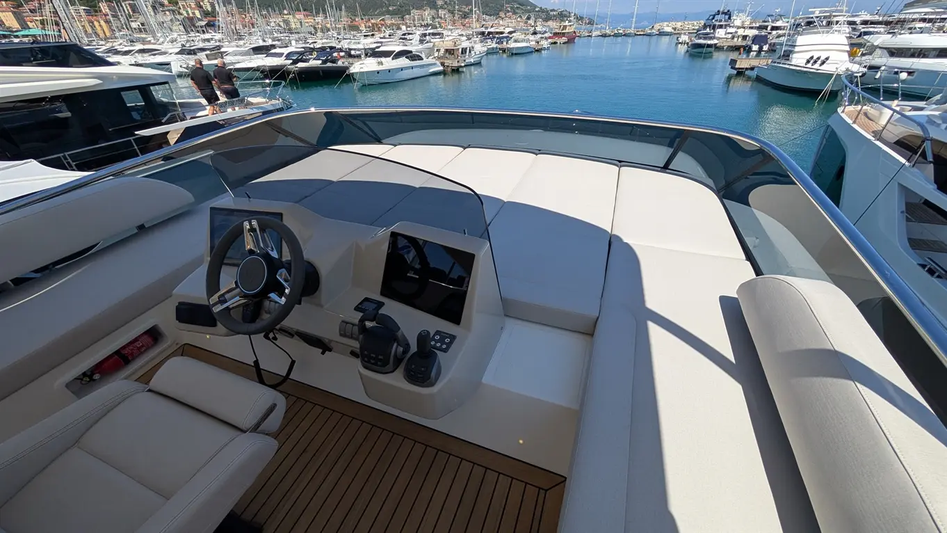 View of a boat's modern helm with a steering wheel, control panel, and comfortable seating, overlooking a marina.